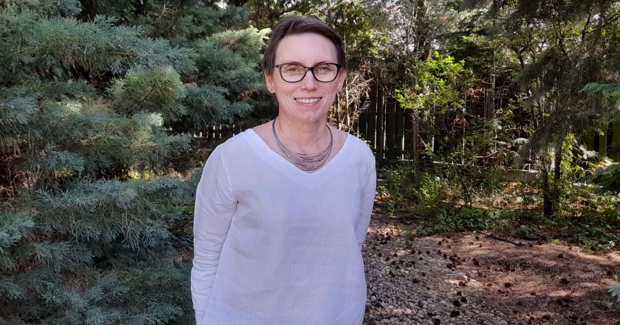 Dr hab. Katarzyna Więckowska, prof. UMK Zdjęcie kobiety w okularach na tle drzew iglastych