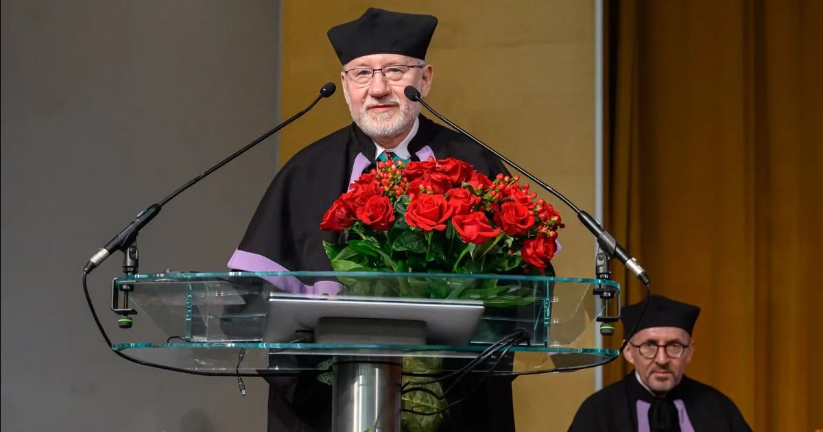 Prof. Witkowski stoi za mówinicą, trzyma bukiet róż