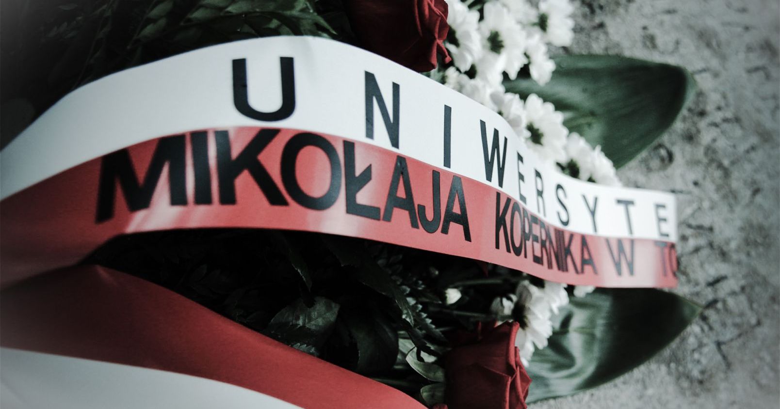  Wiązanka kwiatów z biało-czerwoną szarfą z napisem Uniwersytet Mikołaja Kopernika w Toruniu
